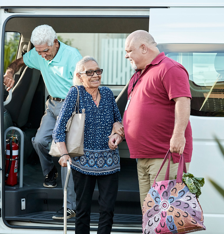 Healthcare worker helping two elderly people step out of van