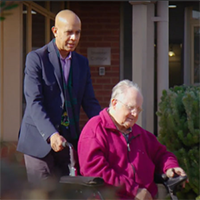 an image of Hans, an older man in a wheelchair, with Aged Care Volunteer Visitor's scheme volunteer, Rahman, enjoying the outdoors.