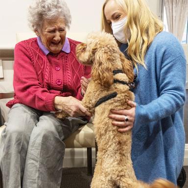 A picture of Betty, an older woman, and Sarah, a community visitor scheme volunteer, petting a dog.