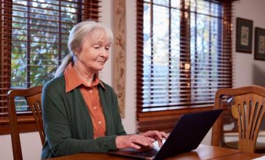 Image description: a woman sitting at a table, with a laptop in front of her.