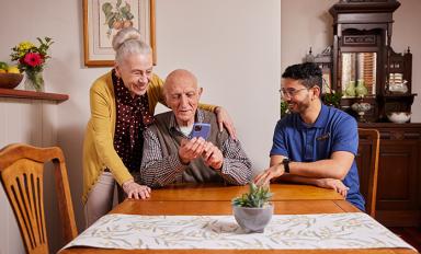 Image Description: an older man and woman at a table with an aged care worker